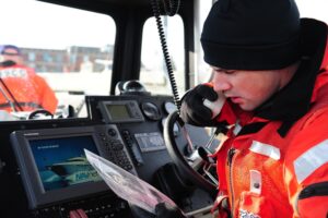 When Language and Accents Complicate Communication at Sea Coast Guard coxswain speaking into a handheld radio on a boat